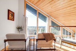 A room with two chairs, a table, and a view through large windows. - Blue Sage No. 8 - The Diagonal Treehome (Fredericksburg)