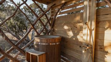 Un sauna extérieur en bois, équipé d’un bain à remous, de bancs et d’un espace douche.