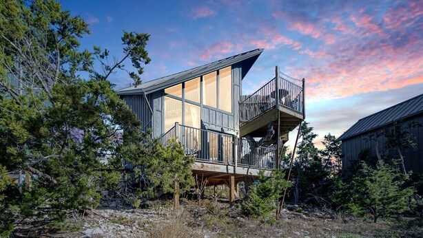 Une maison moderne à deux étages, dotée d’un balcon, entourée d’arbres et offrant une vue sur un ciel dégagé.