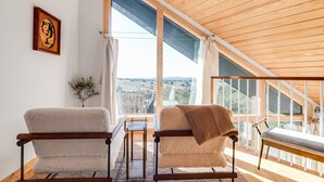 Une pièce chaleureuse avec deux fauteuils, une petite table et une vue sur la campagne, grâce à de grandes fenêtres.