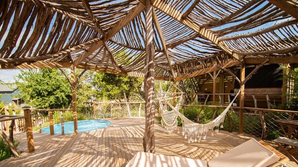 Une terrasse en bois avec une piscine, des chaises longues et un hamac.