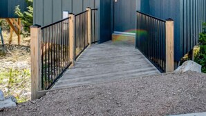 A modern building with a dark blue exterior, a wooden deck leading to a door, and a metal railing. - Blue Sage No. 9 - The Stairway to Heaven (Fredericksburg)
