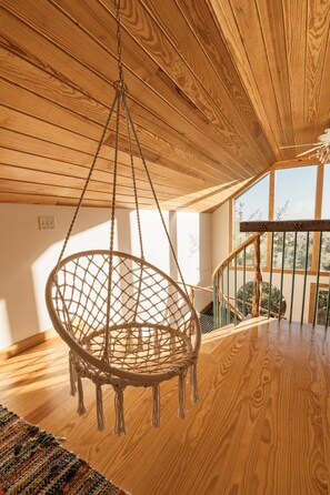 A room with a wooden ceiling, a macramé hanging chair, and a staircase leading to an outdoor area.