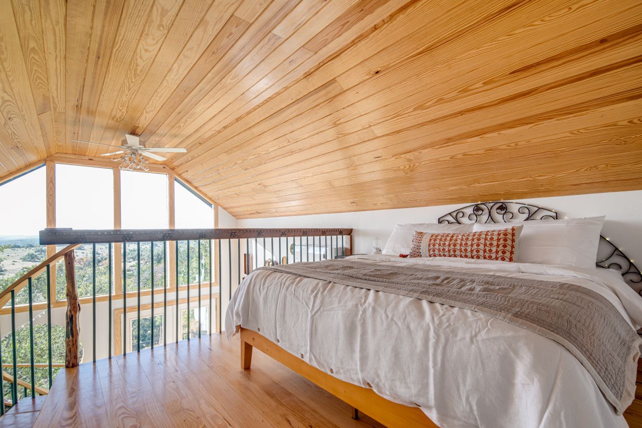 Un dormitorio con techo de madera, una cama con ropa de cama blanca y un balcón con barandilla.
