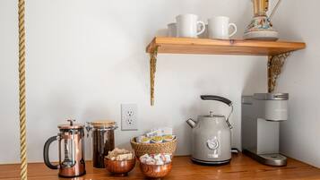 A kitchen counter with a coffee maker, a kettle, a coffee pot, and a shelf with cups and a decorative pitcher.
