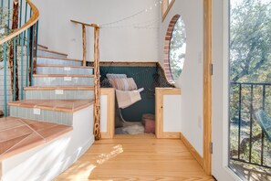 A spiral staircase with a view of a cozy nook with a hammock and a window overlooking greenery.