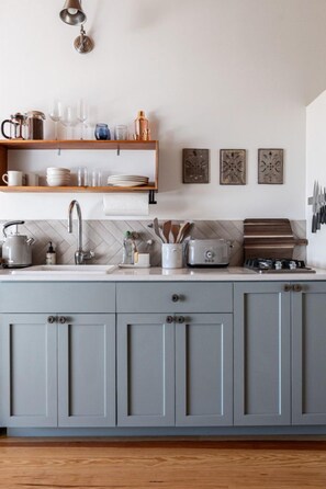 A kitchen with grey cabinets, a white countertop, a kettle, a toaster, and a hanging knife set.