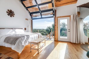 Une chambre avec un grand lit, un banc, un balcon avec vue et un plafond en bois.