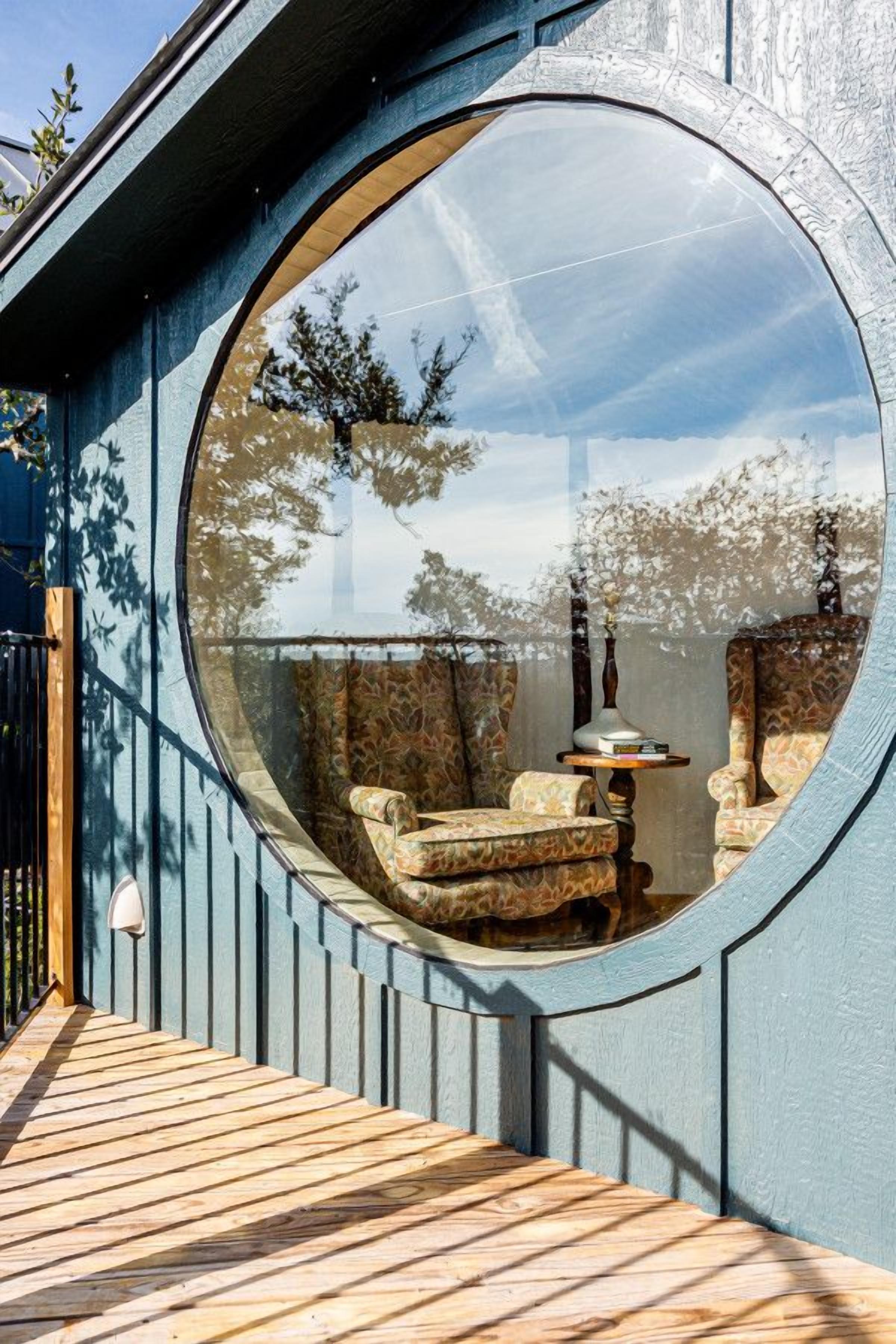 Ein rundes Fenster mit Blick auf Gartenmöbel und einen Baum.