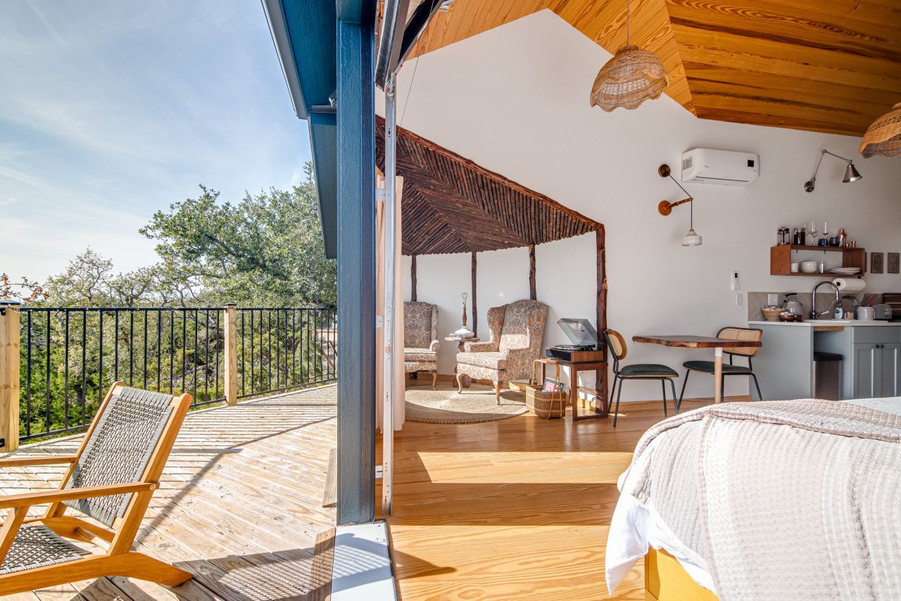 A spacious balcony with wooden flooring, a seating area with a table and chairs, and a bedroom with a bed and a desk.