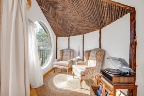 A cozy room with a round window, two patterned armchairs, a wooden side table, and a record player. - Blue Sage No. 10 - The Round Window Treehome (Stair-Free!) (Fredericksburg)