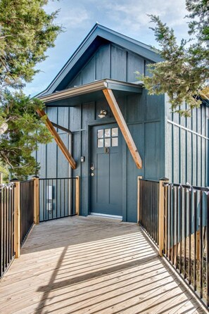 Une terrasse en bois mène à un bâtiment bleu foncé doté d’une porte et de fenêtres.