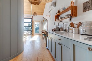 A kitchen with wooden cabinets, a white countertop, and a hanging light fixture. - Blue Sage No. 10 - The Round Window Treehome (Stair-Free!) (Fredericksburg)