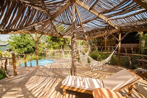 A wooden deck with a pool, lounge chairs, and a hammock.