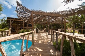 A wooden deck with a pool, wooden pergolas, and hammocks.