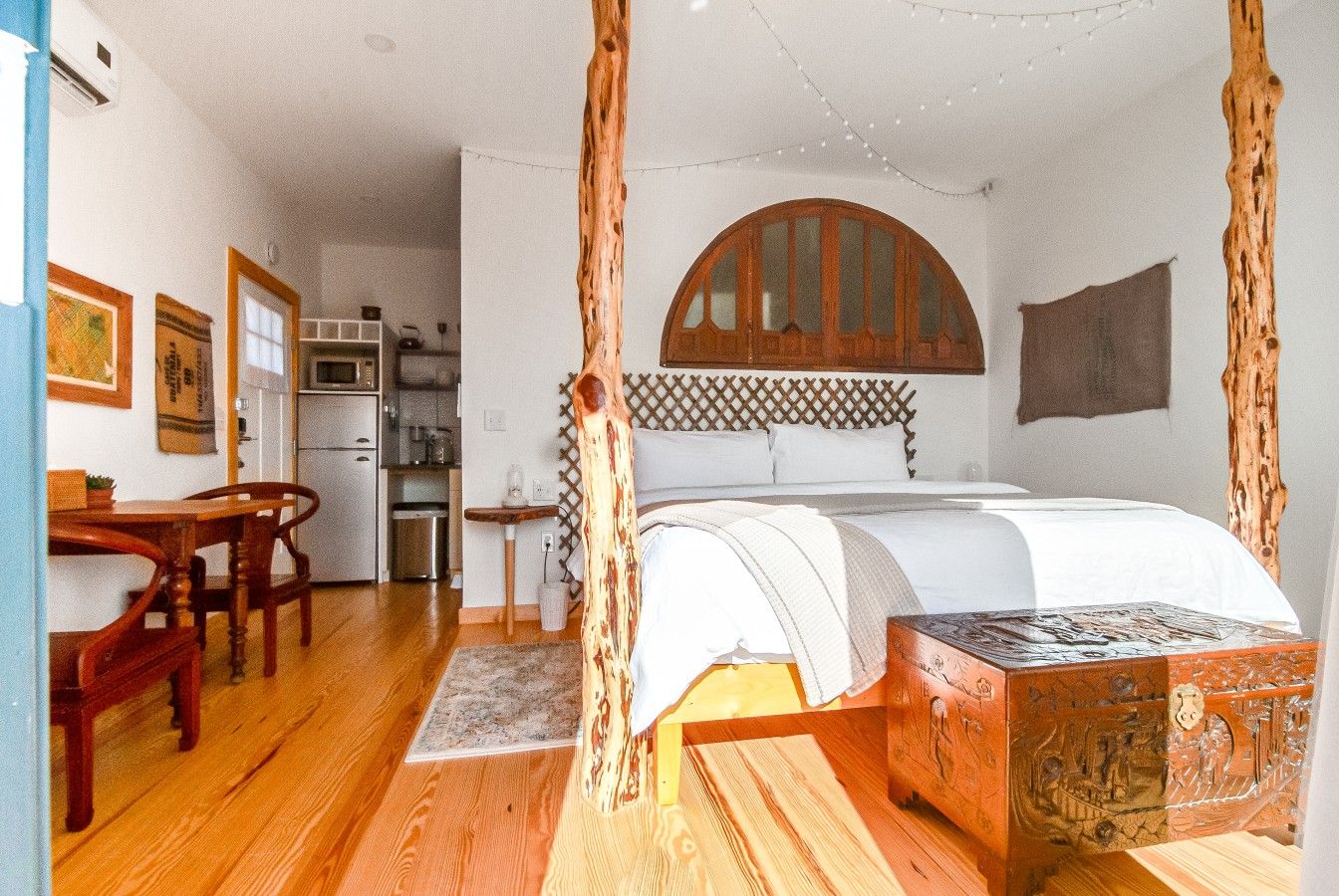 Una habitación con cama, muebles de madera, una zona de cocina y un cabecero decorativo de madera.
