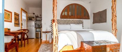 Una habitación con cama, muebles de madera, una zona de cocina y un cabecero decorativo de madera.