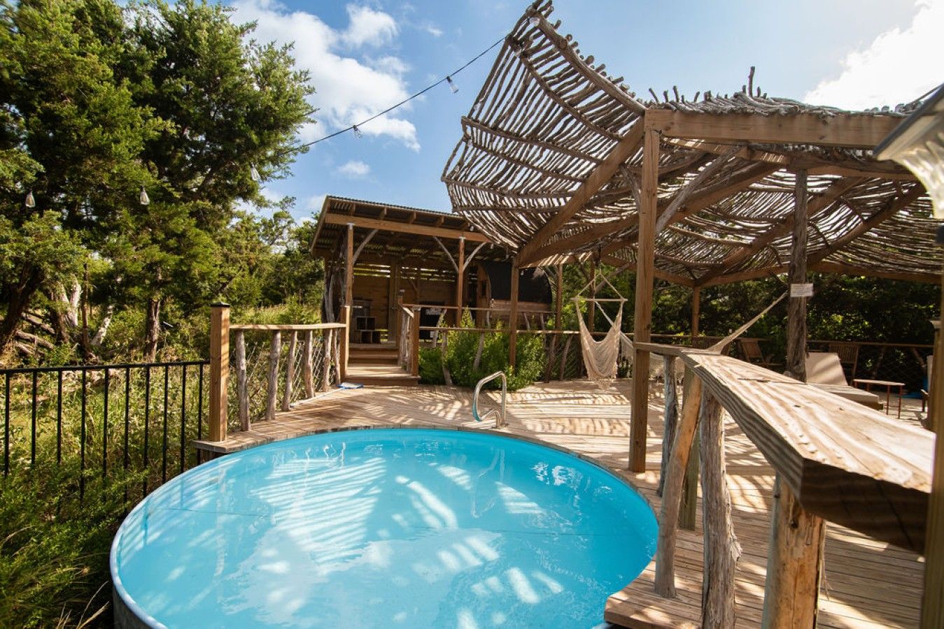 A wooden deck with a pool, a covered seating area, and a hammock.