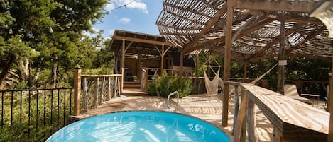 A wooden deck with a pool, a covered seating area, and a hammock.
