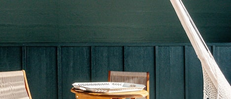 A hammock, two wooden chairs, and a small table outside a building with a dark green facade.