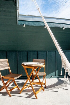 A hammock, two wooden chairs, and a small table outside a building with a dark green facade.