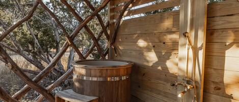 A wooden outdoor sauna with a hot tub, benches, and a shower area.