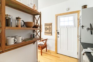 Una cocina con estantes de madera, cafetera, tetera y una ventana con cortina.
