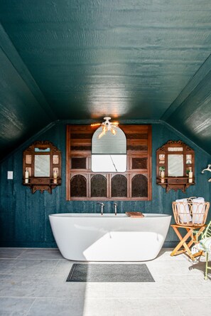 Un baño con una bañera independiente, apliques de pared de madera y un espejo sobre la bañera.
