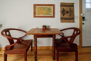 A wooden dining table with two chairs, a framed artwork on the wall, and a burlap sack with text.