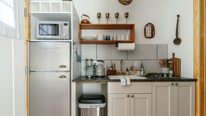 Une cuisine compacte équipée d’un réfrigérateur en acier inoxydable, d’un four à micro-ondes, d’un évier et d’une étagère en bois au-dessus du plan de travail.