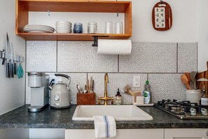 Una cocina con cafetera, tetera, lavabo y diferentes utensilios.