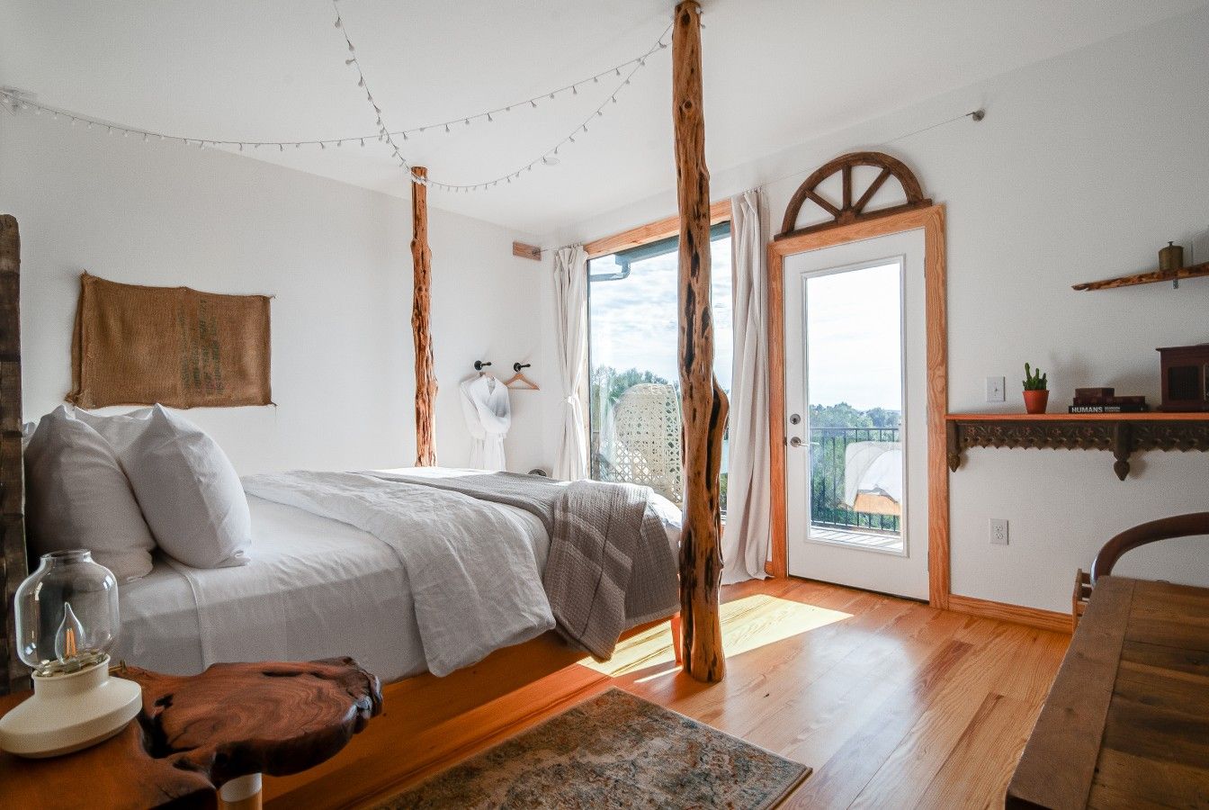 Un dormitorio con cama, piso de madera, ventana y puerta que da al exterior.