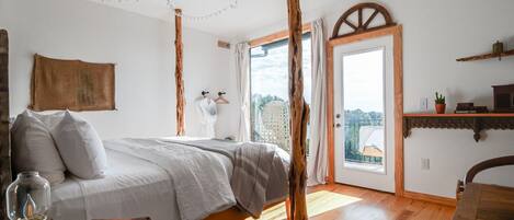 A bedroom with a bed, a wooden floor, a window, and a door leading outside.