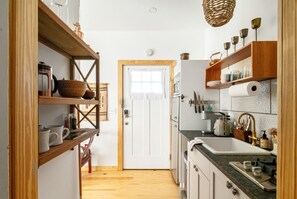 A narrow kitchen with wooden shelves, a white door, and a countertop with a sink. - Blue Sage No. 11 - The Rooftop Stargazer (Fredericksburg)