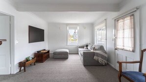 Un salón amplio con un sofá gris, un banco de madera y un televisor montado en la pared.