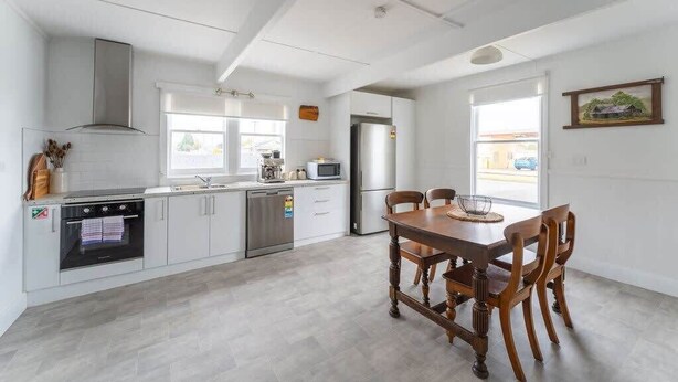 Una cocina moderna con armarios blancos, una mesa de comedor de madera y un refrigerador.