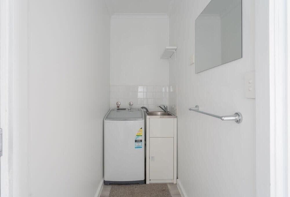 A small, white bathroom with a sink, a mirror, and a refrigerator.