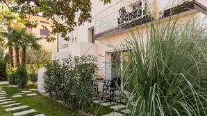 A modern outdoor patio area with a stone pathway, lush greenery, and a seating area with a table and chairs. - CENTURY 1 APARTMENTS " SAN MARCO" (Peschiera del Garda)