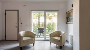 A room with two beige armchairs, a door, and a sliding glass door leading to an outdoor area with a table and chairs. - CENTURY 1 APARTMENTS " SAN MARCO" (Peschiera del Garda)