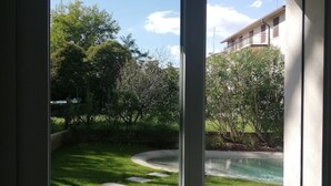 A view through a window of a backyard with a swimming pool, stone pathway, and surrounding greenery. - CENTURY 1 APARTMENTS " SAN MARCO" (Peschiera del Garda)