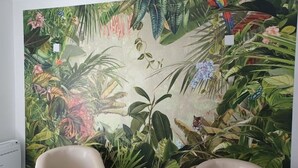 Une pièce avec un grand décor mural aux motifs tropicaux, deux chaises blanches et un radiateur blanc.