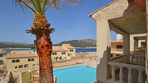 A pool with a clear view of the sea and mountains in the background, a palm tree, and a building with a stone facade. - Perleta - Apartment with sea views and communal pool in Mallorca (Capdepera)