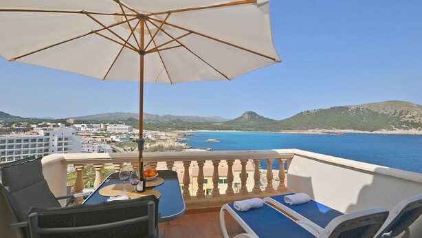 A balcony with a table, chairs, and an umbrella overlooking a coastal view. - Perleta - Apartment with sea views and communal pool in Mallorca (Capdepera)