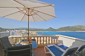 A balcony with a table, chairs, and an umbrella overlooking a coastal view. - Perleta - Apartment with sea views and communal pool in Mallorca (Capdepera)