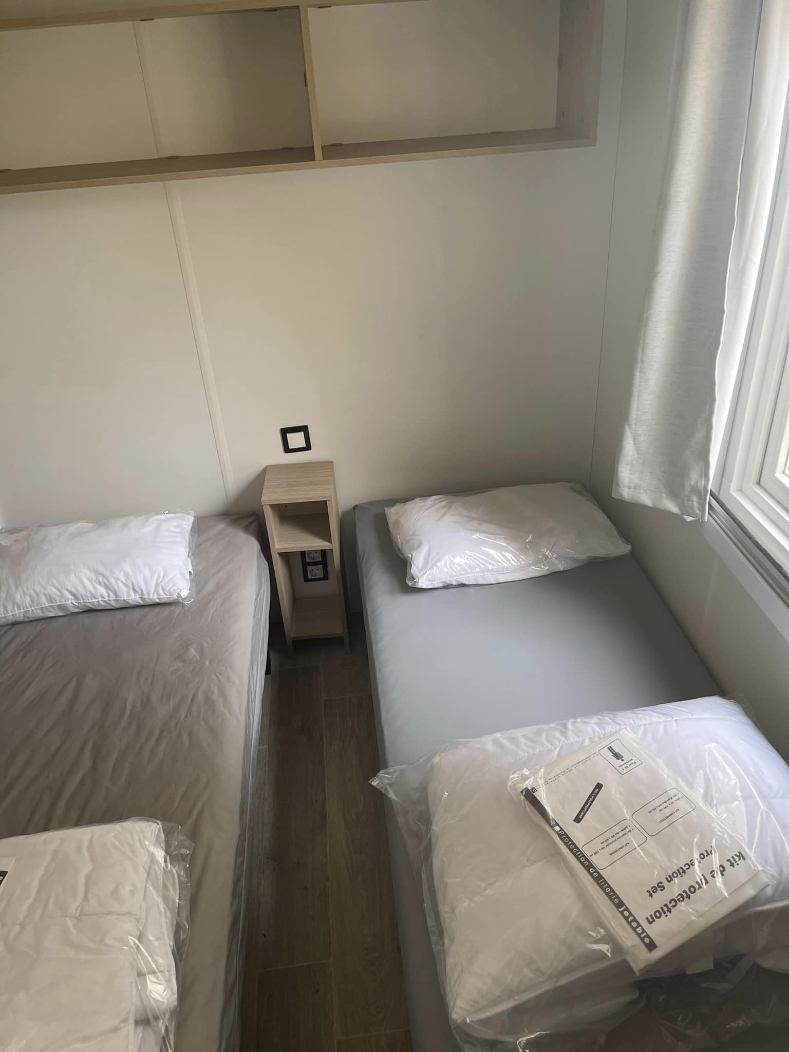 A small, compact room with two beds, a nightstand, and a window.