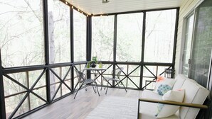 Een ruim balkon met een houten vloer, een witte bank met kussens en een kleine tafel met stoelen.