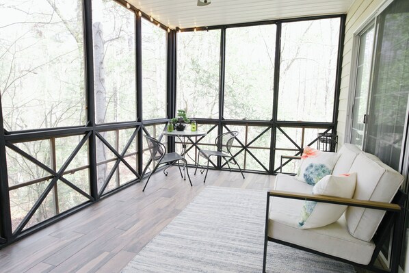 A spacious balcony with a wooden floor, a white sofa with cushions, and a small table with chairs.