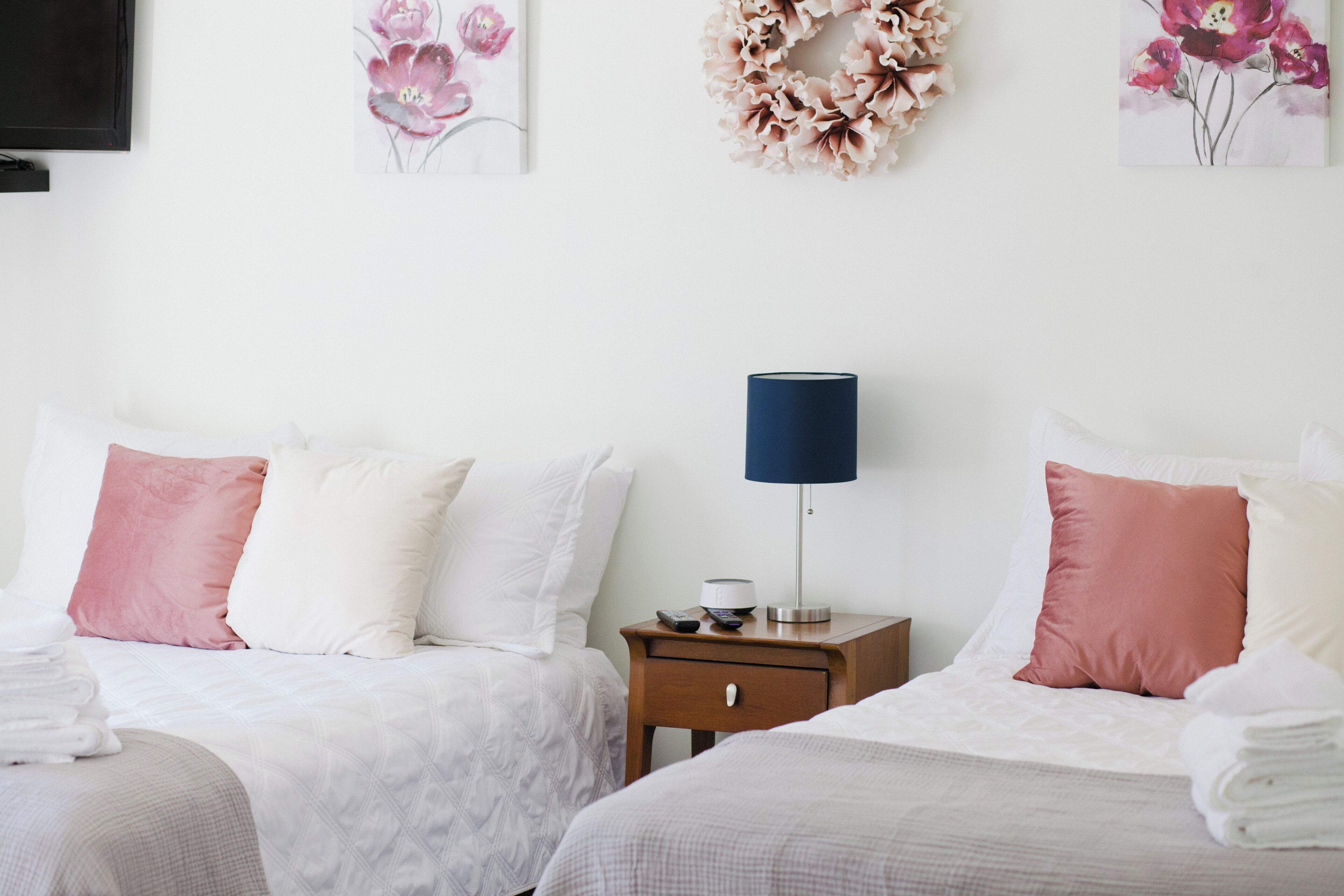 Een hotelkamer met twee bedden, elk voorzien van witte beddengoed en roze kussens. Er staat een nachtkastje met een lamp en een afstandsbediening.