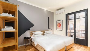 A modern bedroom with a wooden bed, a built-in shelf with towels, a small round table, and a large window with a balcony view. - Vista: Spacious city centre home (Thessaloniki)