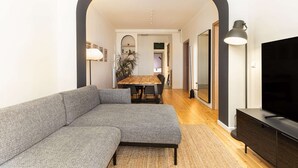 A modern living room with a sectional sofa, a dining table, and a TV. - Vista: Spacious city centre home (Thessaloniki)